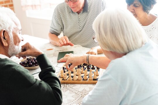 Group of seniors playing chess at a table. Elderly friends enjoying a chess game. Seniors, chess, and friendship in a cozy setting. Engaged in strategic play. Senior people playing chess.