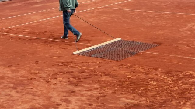 Worker using a specialized tool to smooth the surface of a clay tennis cour