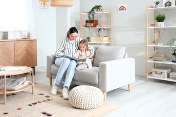 Young woman reading story to her little daughter at home
