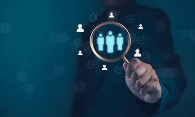 A person holds a magnifying glass over digital icons representing people, symbolizing focus on human resources or talent acquisition.