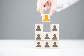 A hand places a distinctive orange avatar on a stack of blocks featuring various human icons, symbolizing leadership and team building.