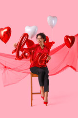 Young African-American woman with Cupid's wings and word LOVE made of balloons on pink background. Valentine's Day celebration