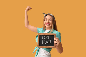 Happy young pin-up woman holding chalkboard with text GIRL POWER and showing her muscles on yellow...