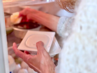 冷蔵庫に納豆パックを入れる高齢女性の手