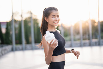 Sporty asian woman in sportswear drinking protein shake from bottle After Exercise for Energy Vitality in morning park sportswoman wellness health.