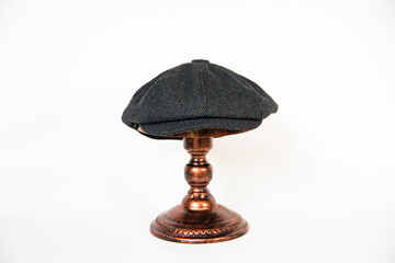 Detail of a black herringbone newsboy hat mounted on a bronze mannequin head on a white background. concept photo of a classic newsboy hat in jet black on a bronze mannequin