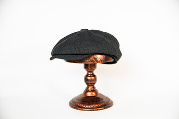 Detail of a black herringbone newsboy hat mounted on a bronze mannequin head on a white background. concept photo of a classic newsboy hat in jet black on a bronze mannequin