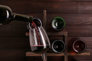 Pouring of red wine from bottle into glass on wooden background