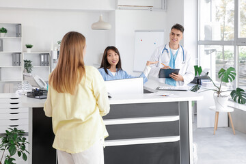 Medical intern working with patient and doctor at reception in clinic