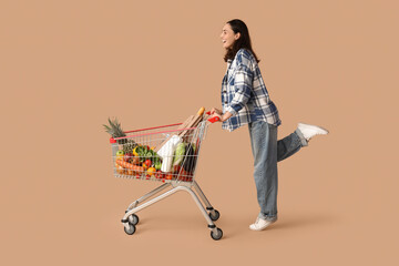 Beautiful young happy woman with full shopping cart on beige background © Pixel-Shot