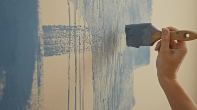 Woman painting blue wall with brush in new home interior, showcasing creative decoration and diy project in cozy apartment setting with emphasis on texture and color detail.