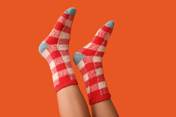 Legs of young woman in warm checkered socks on orange background