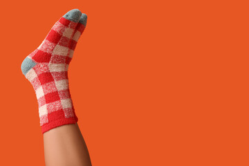 Legs of young woman in warm checkered socks on orange background