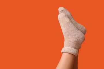 Legs of young woman in warm beige socks on orange background