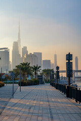  Beautiful waterfront promenade in Dubai Design District with a hazy sunset over Dubai skyline and Burj Khalifa