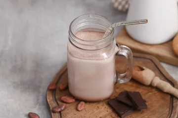 Gardinen Mason jar of sweet chocolate milk and cocoa beans on grey background © Pixel-Shot