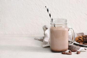 Mason jar of sweet chocolate milk and cocoa beans on white background