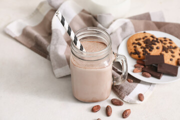 Mason jar of sweet chocolate milk with tasty cookies and cocoa beans on white background