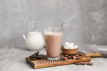 Glass of sweet chocolate milk with cocoa beans and cubes of sugar on grey background