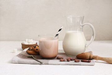 Glass of sweet chocolate milk with tasty cookies and cocoa beans on white background