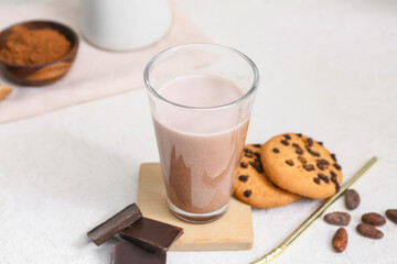 Glass of sweet chocolate milk with tasty cookies and cocoa beans on white background