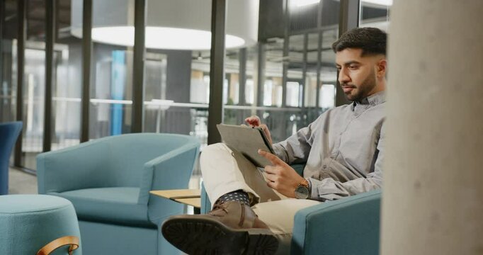 Thinking and holding tablet, businessman sitting in modern office lounge area