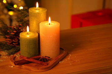 Burning candles, spices, pine cone and coniferous branch on wooden table in evening