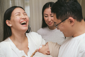 Family embracing cute infant child boy with love in the room. Smiling asian mother, father and aunt...