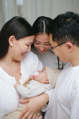 Family embracing cute infant child boy with love in the room. Smiling asian mother, father and aunt holding sleeping newborn baby. Slow-motion. 