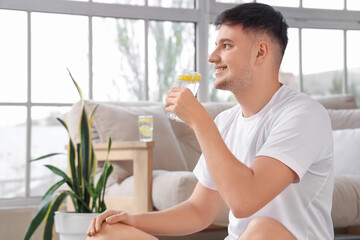 Sporty young man drinking lemon infused water at home