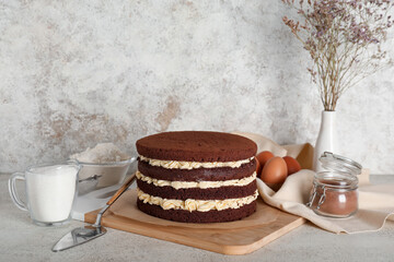 Wooden board with tasty sponge cake, spatula and ingredients on light table
