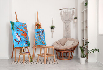Interior of modern artist's workshop with pictures on easels, art supplies and armchair