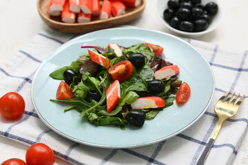 Plate of salad with crab sticks, spinach, black olives and tomatoes on napkin
