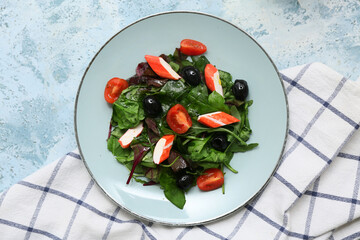 Plate of salad with crab sticks, spinach, black olives and tomatoes on blue grunge background