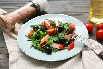 Plate of salad with crab sticks, spinach, black olives and tomatoes on wooden background