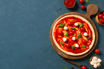 Wooden board with raw pizza with ingredients on turquoise grunge background