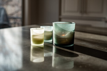Three glass jar candles placed on a reflective surface, lit by natural light and casting soft shadows