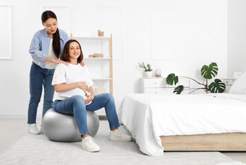 Obraz premium Young Asian doula with pregnant woman training on fitball in bedroom