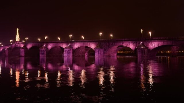 A historic stone bridge illuminated in pink over calm waters at night in Blois, France