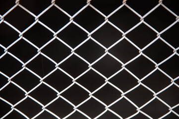 close up view of diamond patterned wire fence with dark background, showcasing intricate design and texture of metal mesh. image evokes sense of confinement and structure