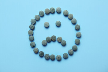 Sad face made of pills on blue background
