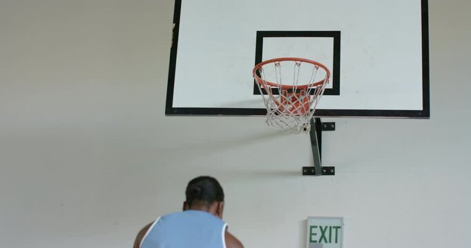 Playing basketball, woman shooting ball towards hoop in indoor court