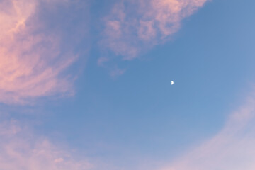 夕暮れの空に浮かぶ月とピンクの雲