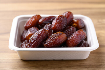 Date palm fruit (MedJool) in biodegradable bowl on wooden background