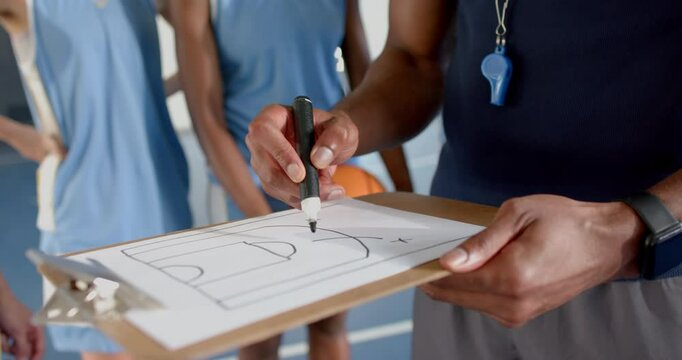 Coach drawing basketball play on clipboard, instructing players on court strategy