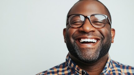 Joyful portrait of a smiling African American man wearing glasses with a checkered shirt against a neutral background