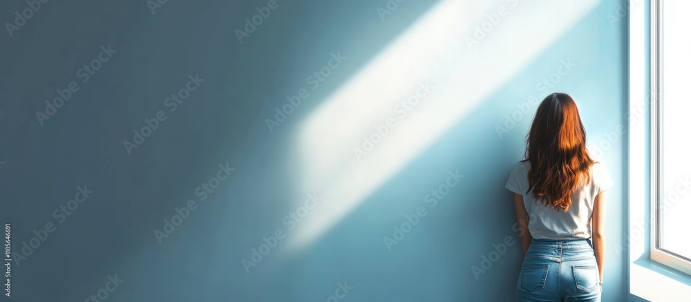 Poster girl standing by a window illuminated by soft natural light with a large empty copyspace on a blue w