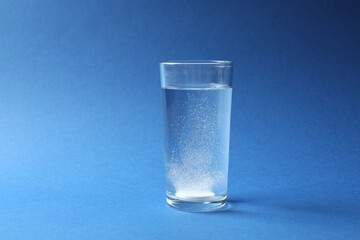 Effervescent pill dissolving in a glas water on blue background 