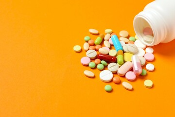 Various pills pouring out of medicine bottle on colorful background