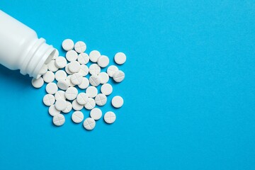 White pills pouring out of medicine bottle on colorful background